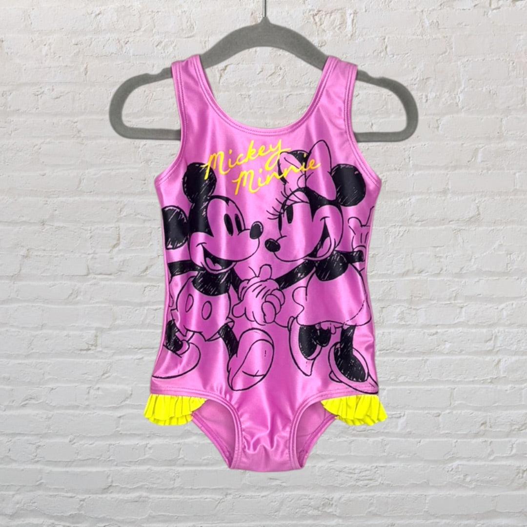 Pink swimsuit featuring a Mickey and Minnie graphic with yellow ruffle details, hanging on a hanger.
