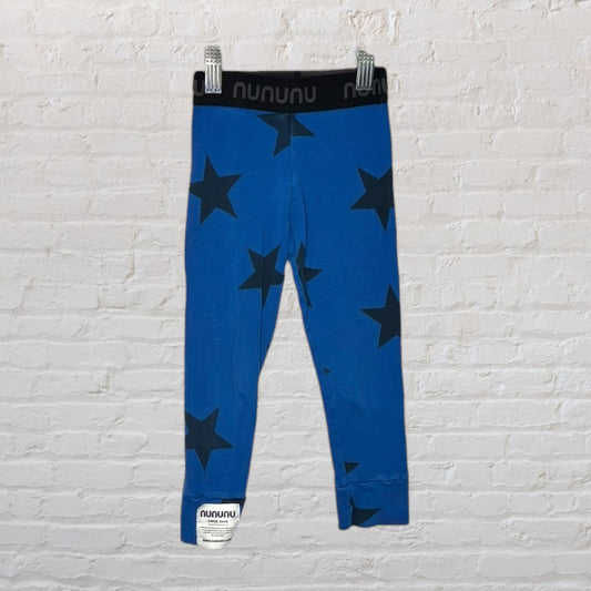 Blue leggings with black star prints and a branded waistband reading 'nununu', hung on a white brick wall background.