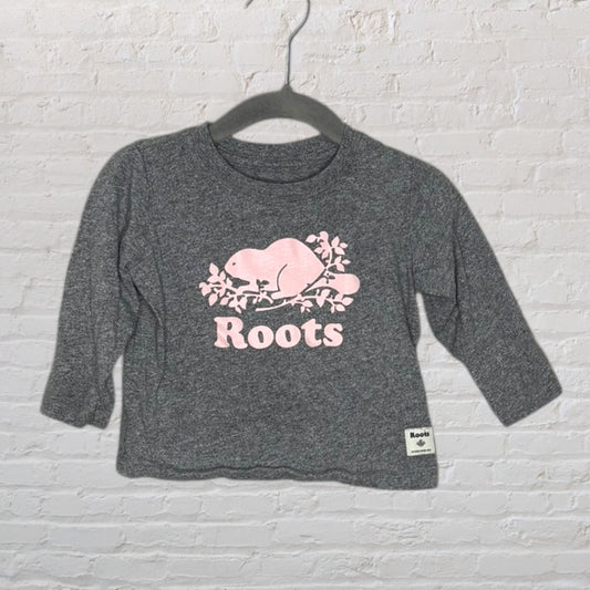 Grey long-sleeve t-shirt with pink Roots beaver logo, hanging on a hanger.