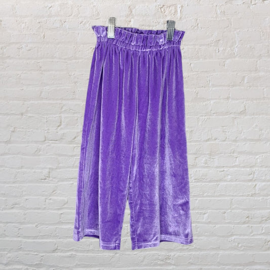 Lavender velvet high-waisted pants with an elastic waistband displayed against a white brick background.