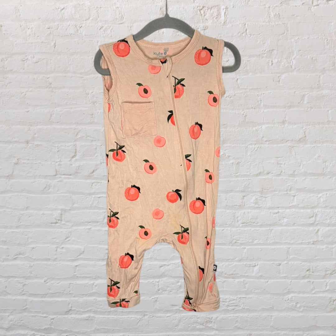 Beige sleeveless romper with peach print and front pocket, hanging on a gray hanger.