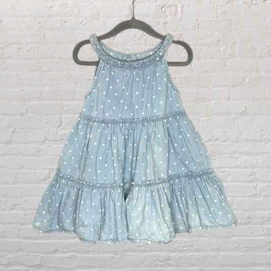 Light blue tiered dress with white star print, hanging on a hanger against a brick wall.