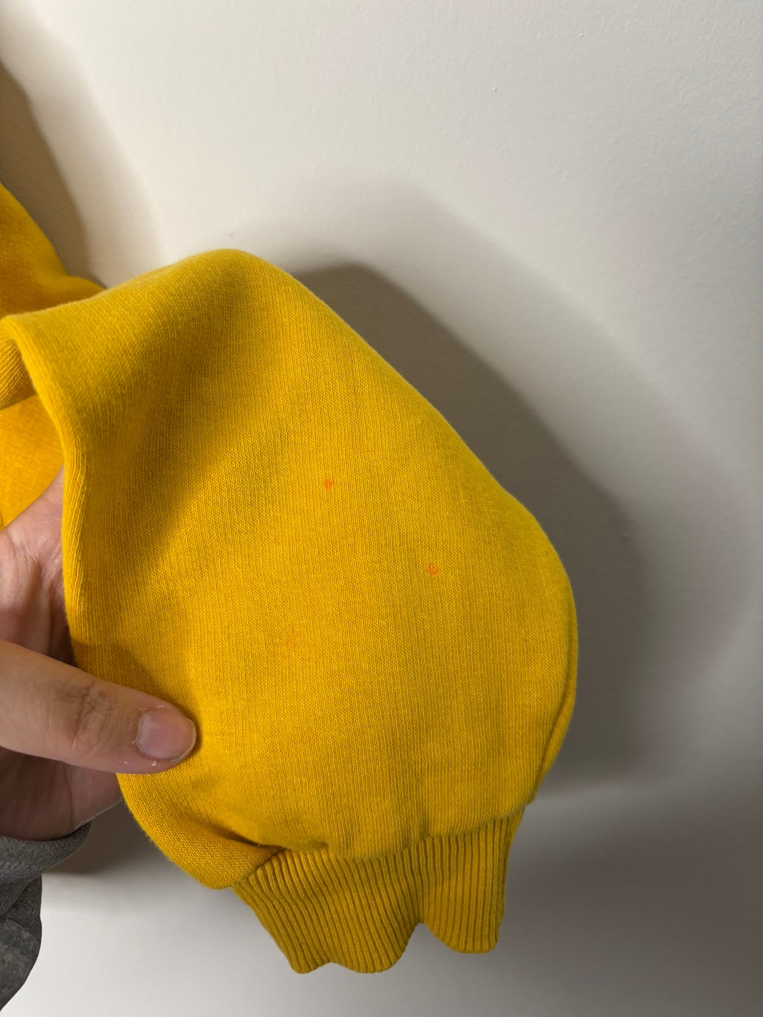 Bright yellow hoodie with drawstring hem and relaxed fit, displayed on a hanger against a white brick wall.