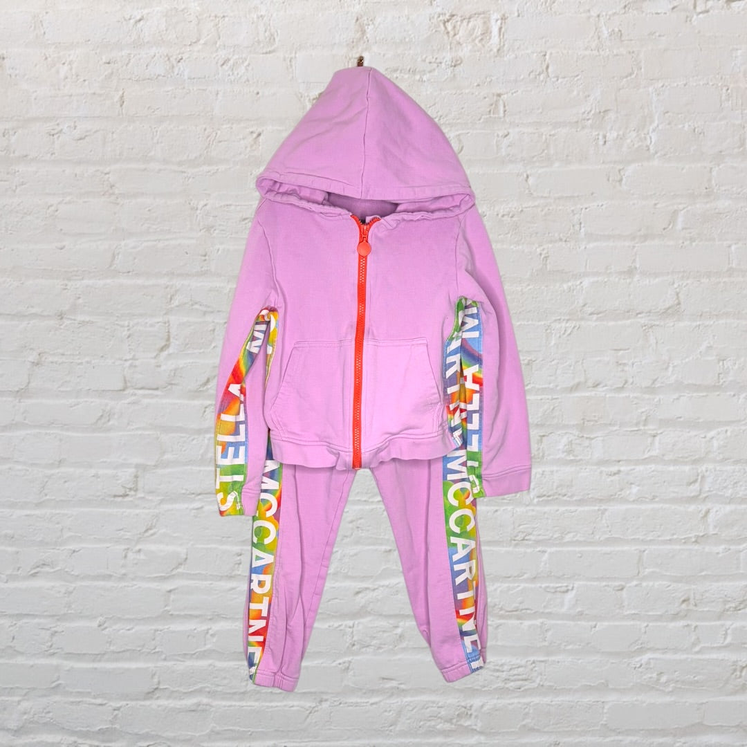 Pink tracksuit set with a hoodie and pants featuring rainbow Stella McCartney logos along the sleeves and legs.