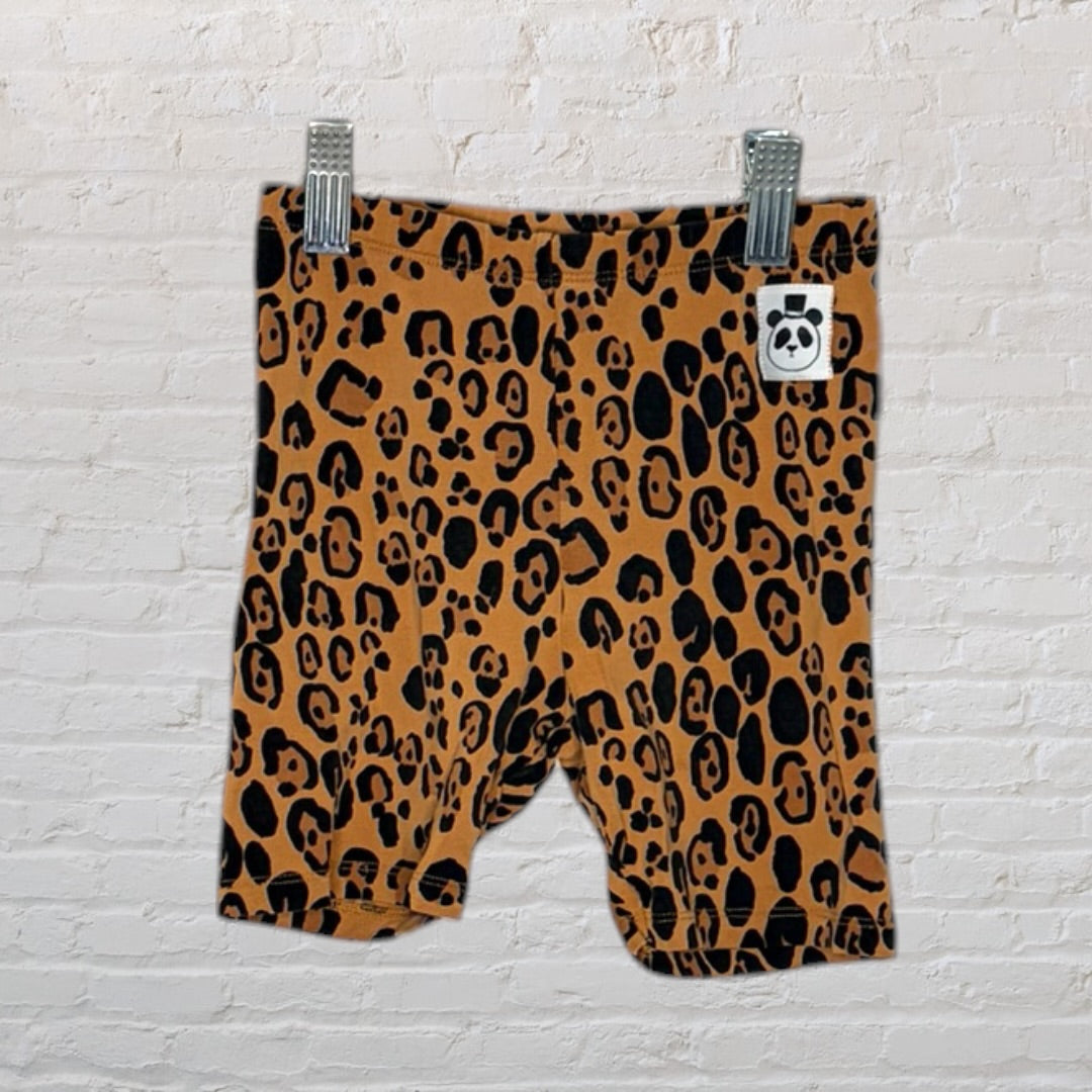 Brown shorts with black leopard print pattern, clipped to a hanger against a brick wall.