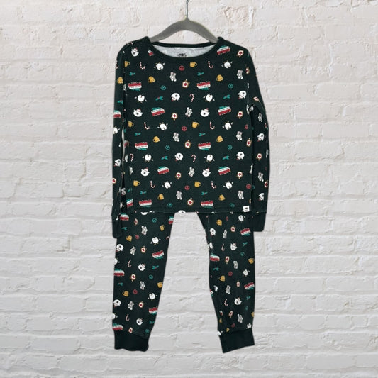 Dark green sleepwear set with festive multicolored patterns hanging on a black hanger against a white brick wall.