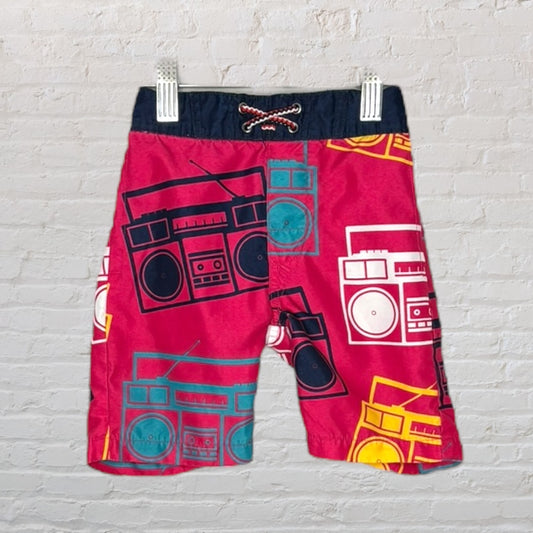 Pink swim trunks with retro boombox prints in various colors, featuring a drawstring waistband.