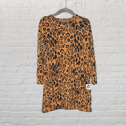 Brown and black leopard print long-sleeve dress hanging on a hanger against a white brick background.