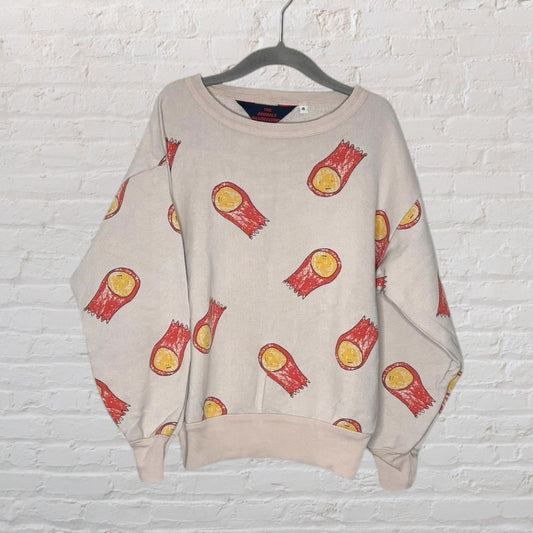 Beige sweatshirt with red and yellow comet print, by The Animals Observatory, hanging against a brick wall.