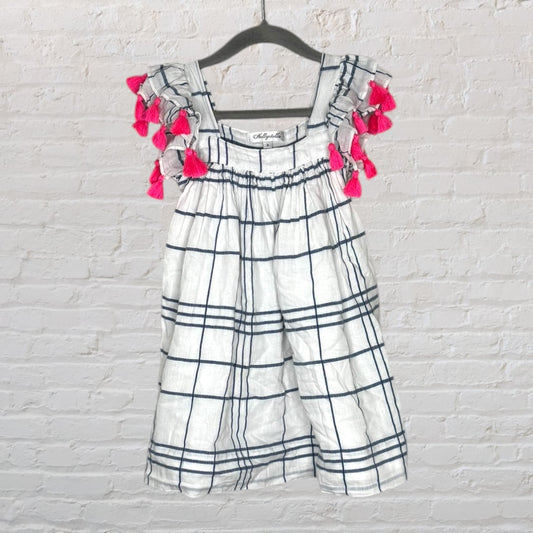 White checkered sleeveless top with navy stripes and pink tassels on the shoulders, hanging on a hanger.