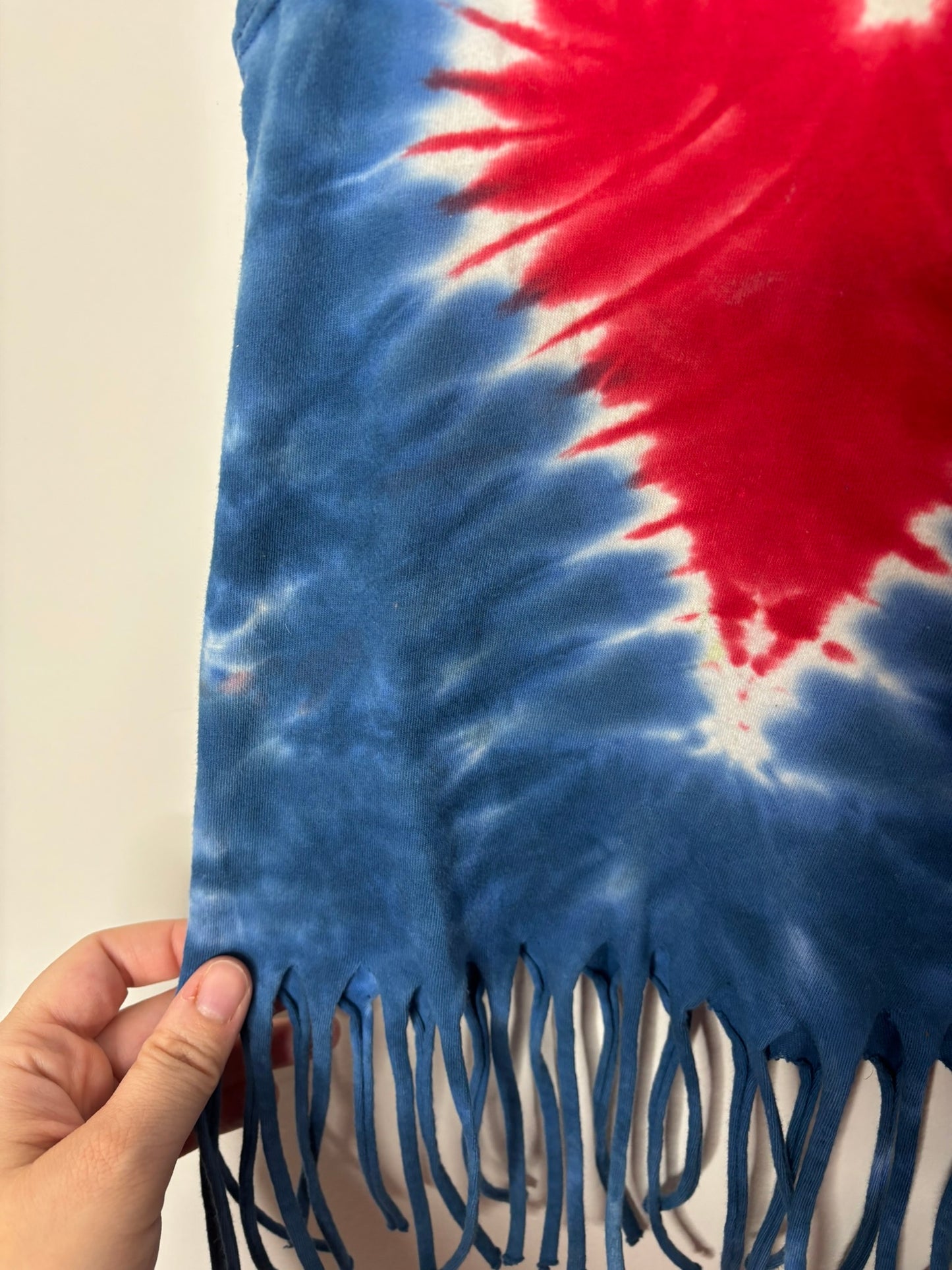 Blue tie-dye tank top with red and white heart design and fringe details at the hem, hanging on a hanger.
