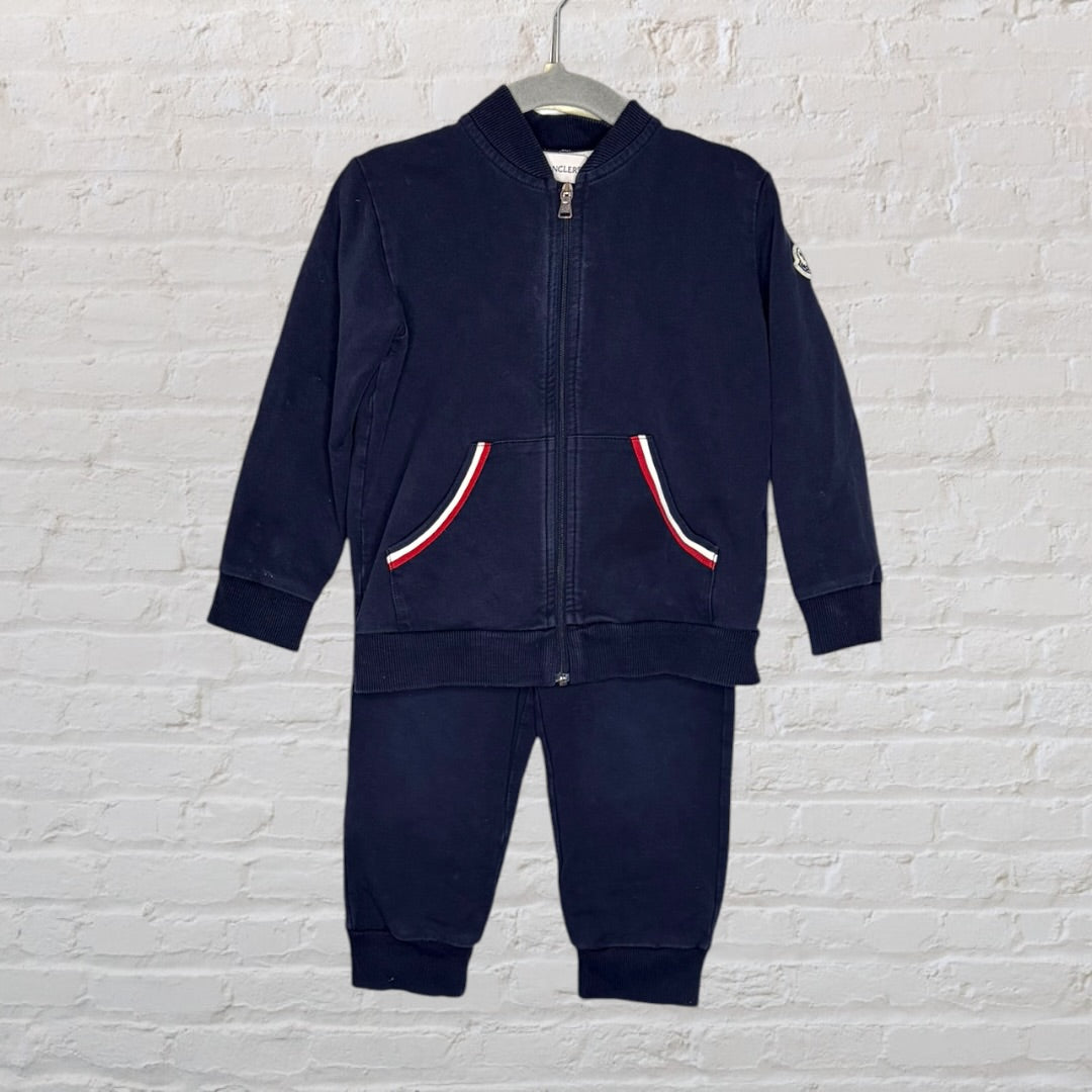 Navy blue Moncler kids' track suit with zip-up jacket and matching pants, featuring red, white, and blue trim detail on pockets.