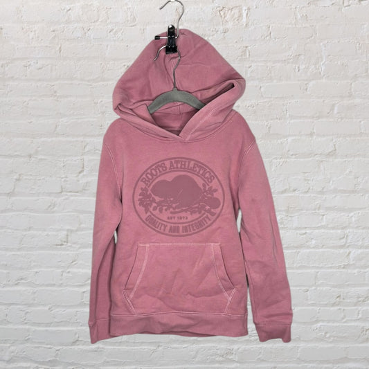 Dusty rose Roots Athletics hoodie with front graphic and kangaroo pocket, hanging against a brick wall.