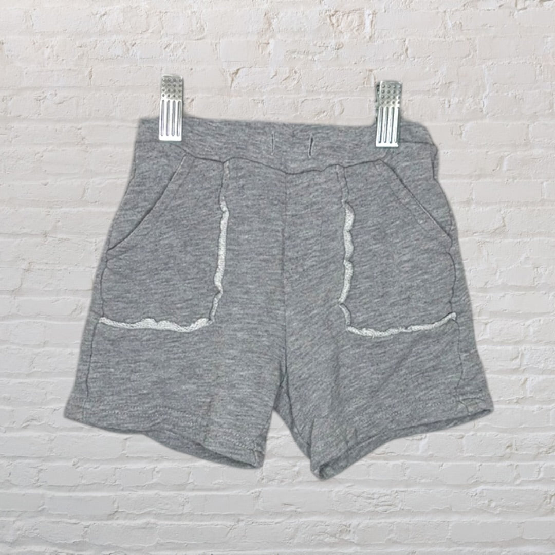 Grey terry shorts with white trim on pockets, hung against a white brick wall.