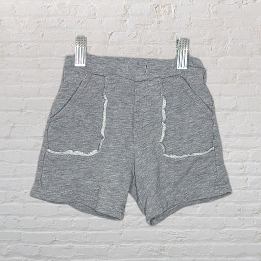 Grey terry shorts with white trim on pockets, hung against a white brick wall.