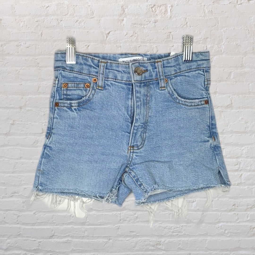 Light blue high-waisted denim shorts with frayed hems hanging against a white brick background.