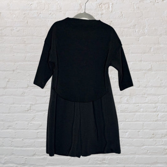 Black dress with 3/4 sleeves and a flared skirt, displayed on a hanger against a white brick wall.