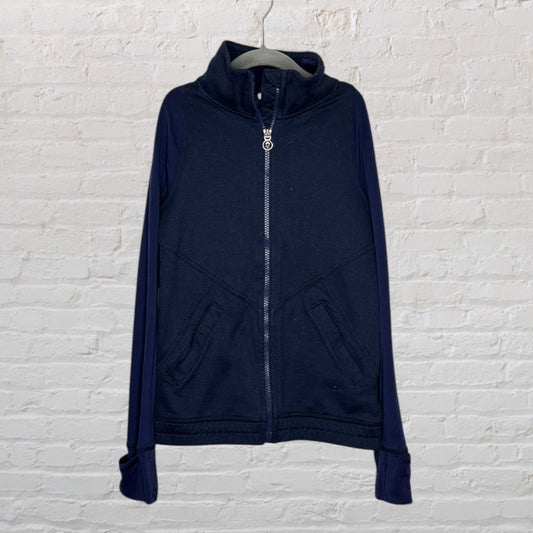Navy blue full-zip jacket with a high neck and front pockets, hanging on a hanger against a white brick wall.
