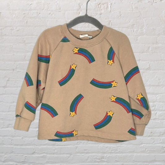 Beige sweatshirt with colorful star and rainbow patterns, hanging on a hanger.