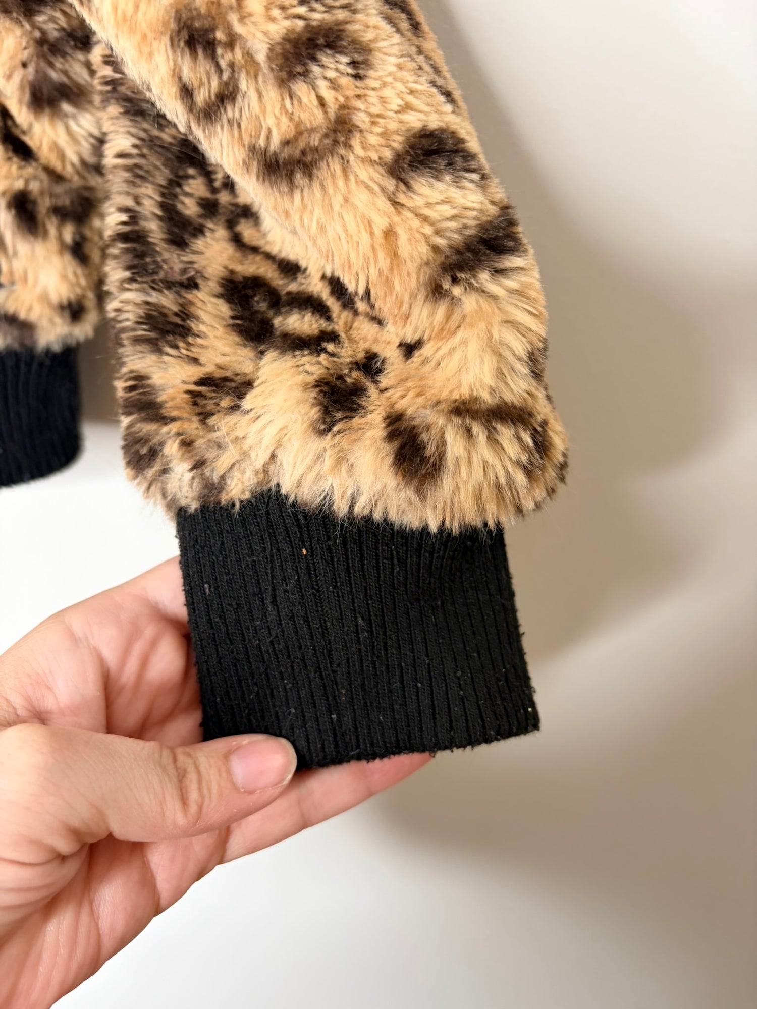 Women's leopard print faux fur jacket with black ribbed cuffs and hem, displayed on a hanger.