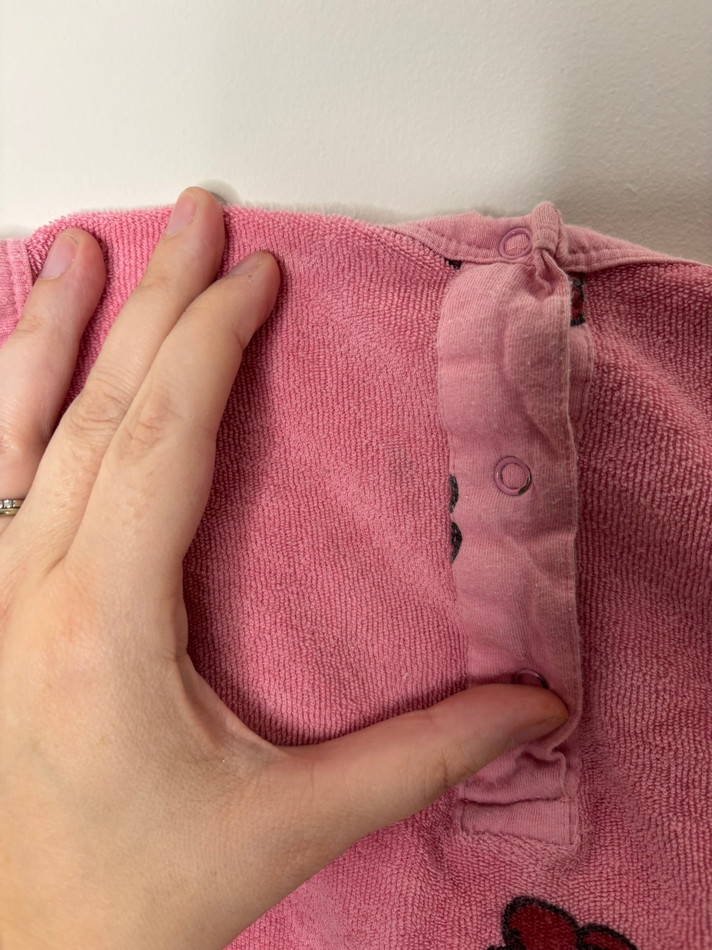 Pink sleeveless romper with button closure and playful printed motifs, hanging on a hanger.