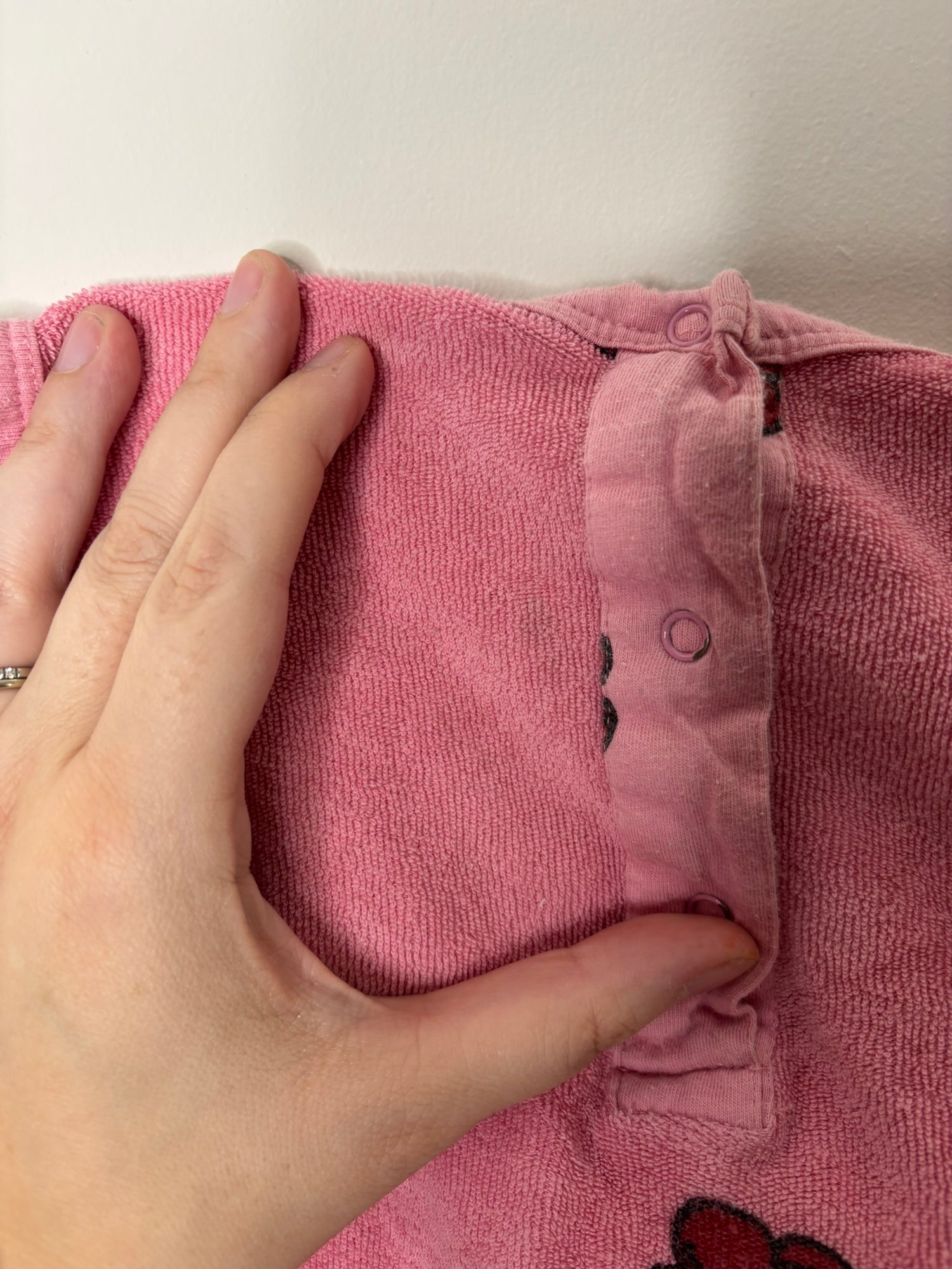 Pink sleeveless romper with button closure and playful printed motifs, hanging on a hanger.