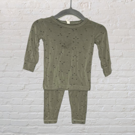 Olive green pajama set with small geometric prints, displayed on a hanger against a brick wall background.