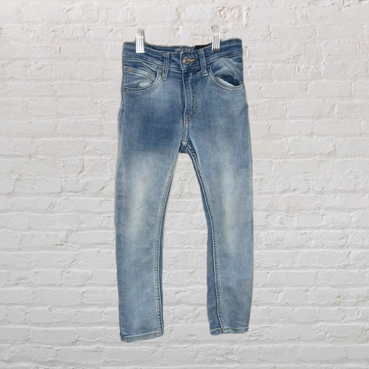 A pair of light blue faded jeans hanging against a white brick wall.