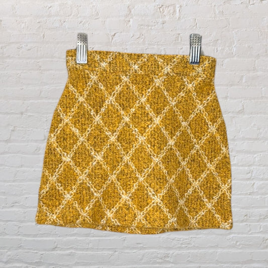 Mustard yellow textured mini skirt with a diamond pattern, clipped on a white brick background.