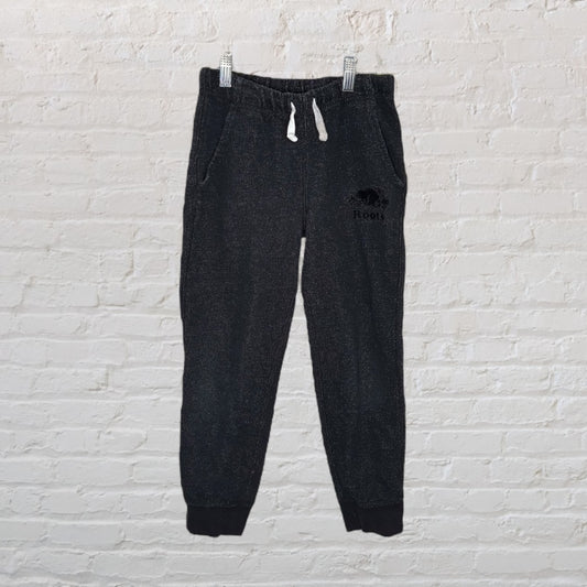 Charcoal colored Roots sweatpants with drawstring and elastic cuffs, displayed against a white brick wall.