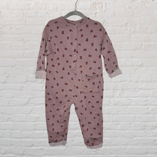 Mauve baby onesie with red and blue floral pattern, featuring long sleeves and cuffed edges, hanging on a hanger.