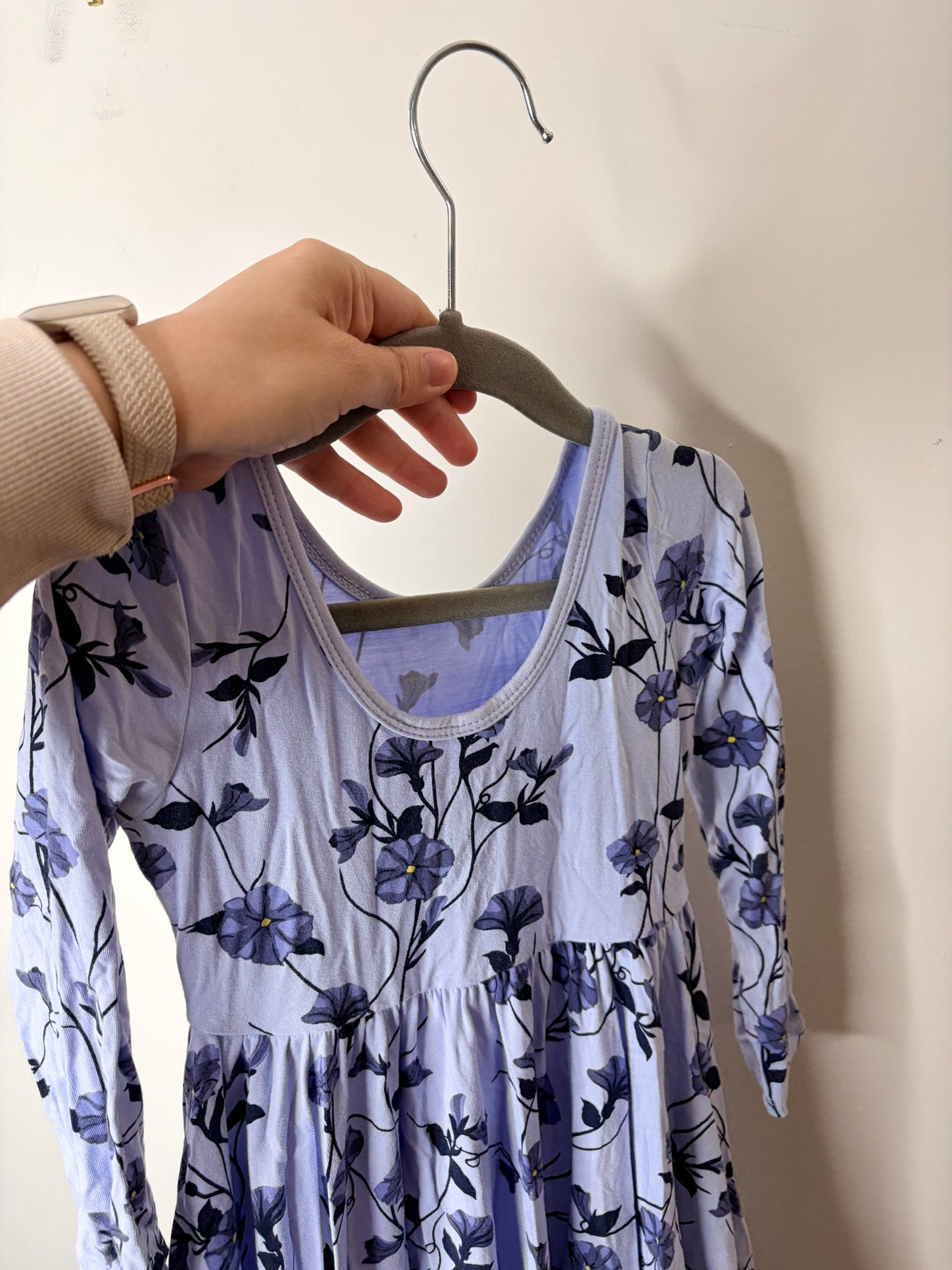 Light blue long sleeve dress with dark floral print, hanging on a white brick wall.