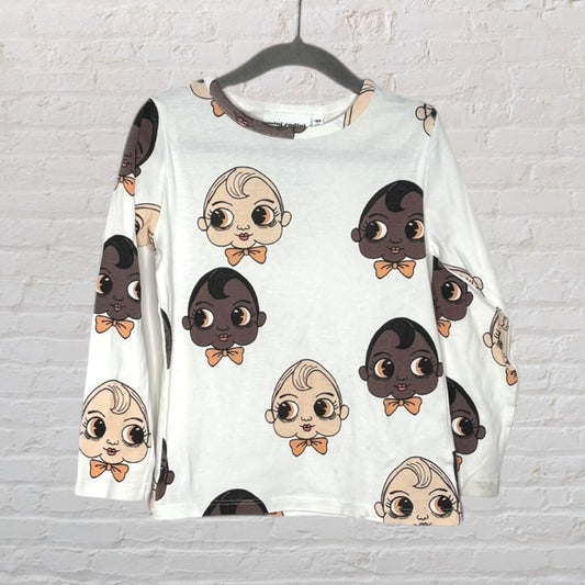 White long sleeve tee with cartoon baby faces in peach and brown tones, displayed on a hanger.