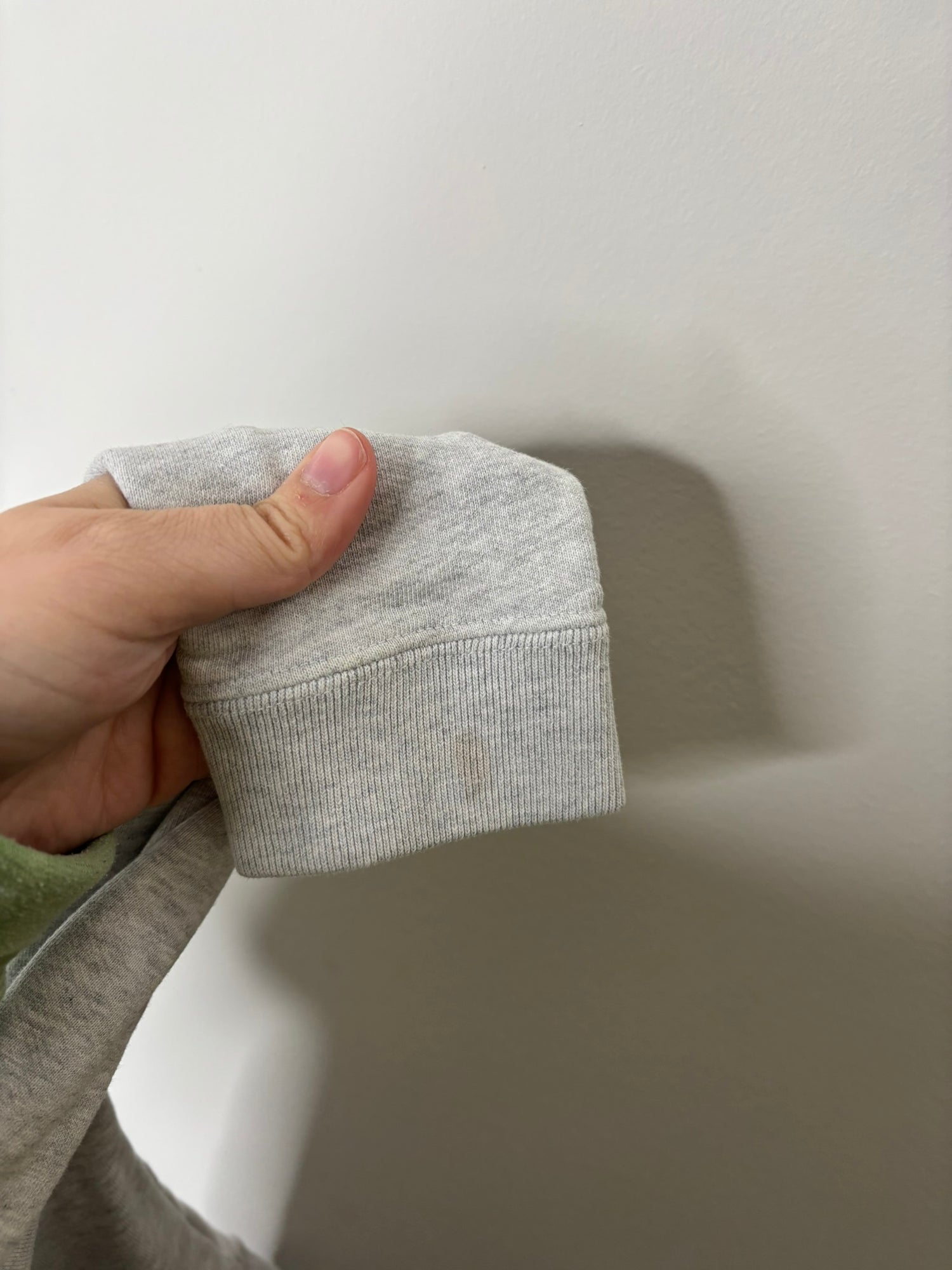 Grey hoodie featuring a small embroidered owl logo on the chest, displayed against a white brick wall.