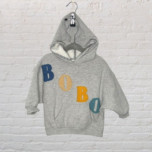 Grey kids' hoodie with colorful 'BOBO' patches, featuring a front pocket and a cozy hood.