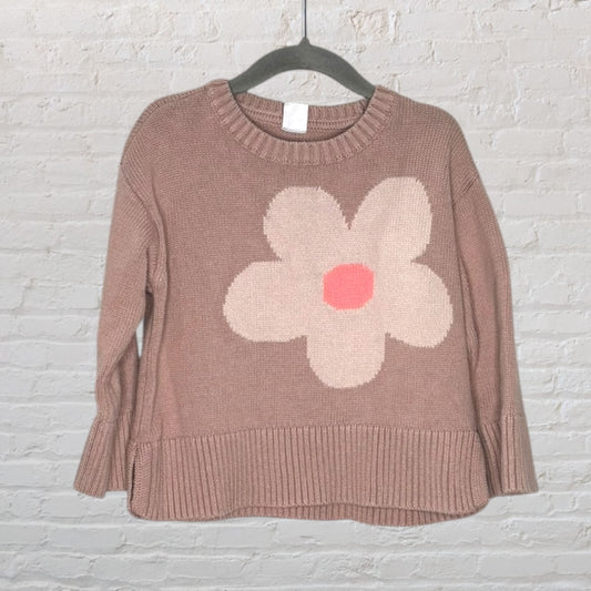 A dusty pink knit sweater featuring a large cream and pink flower design on the front, hanging on a clothes hanger.