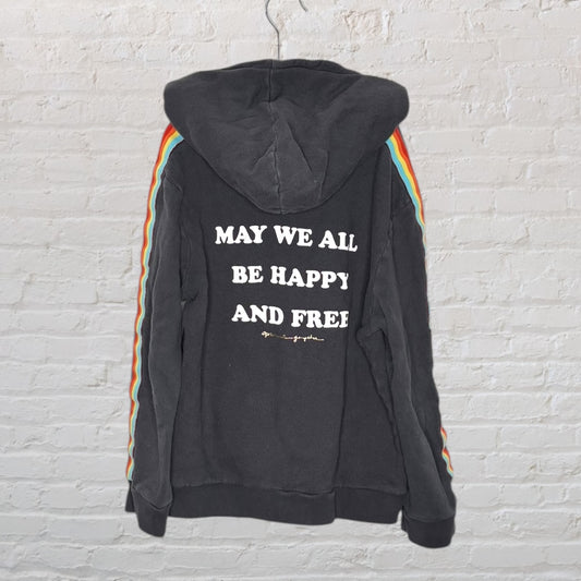 Black hoodie with rainbow stripes on sleeves and 'May We All Be Happy and Free' text on back.