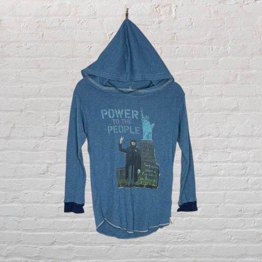 Blue long-sleeve hoodie with 'Power to the People' graphic and image in front, displayed against a brick wall.