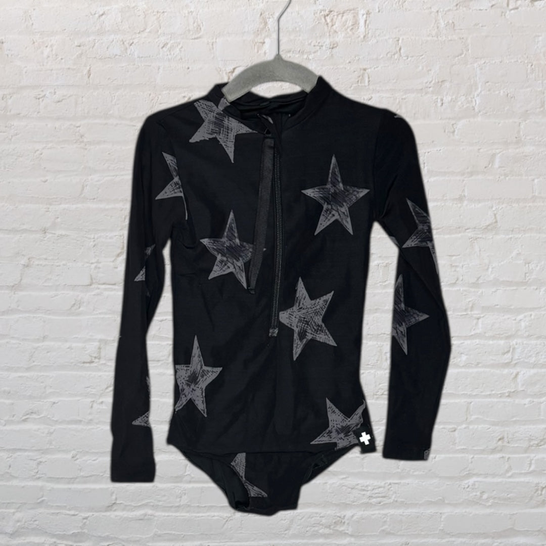 Black long sleeve bodysuit with grey star pattern and front zipper, displayed on a hanger against a brick wall.