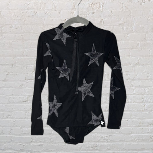 Black long sleeve bodysuit with grey star pattern and front zipper, displayed on a hanger against a brick wall.