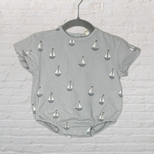 Gray baby romper with sailboat pattern printed all over, displayed on a hanger against a white brick wall.