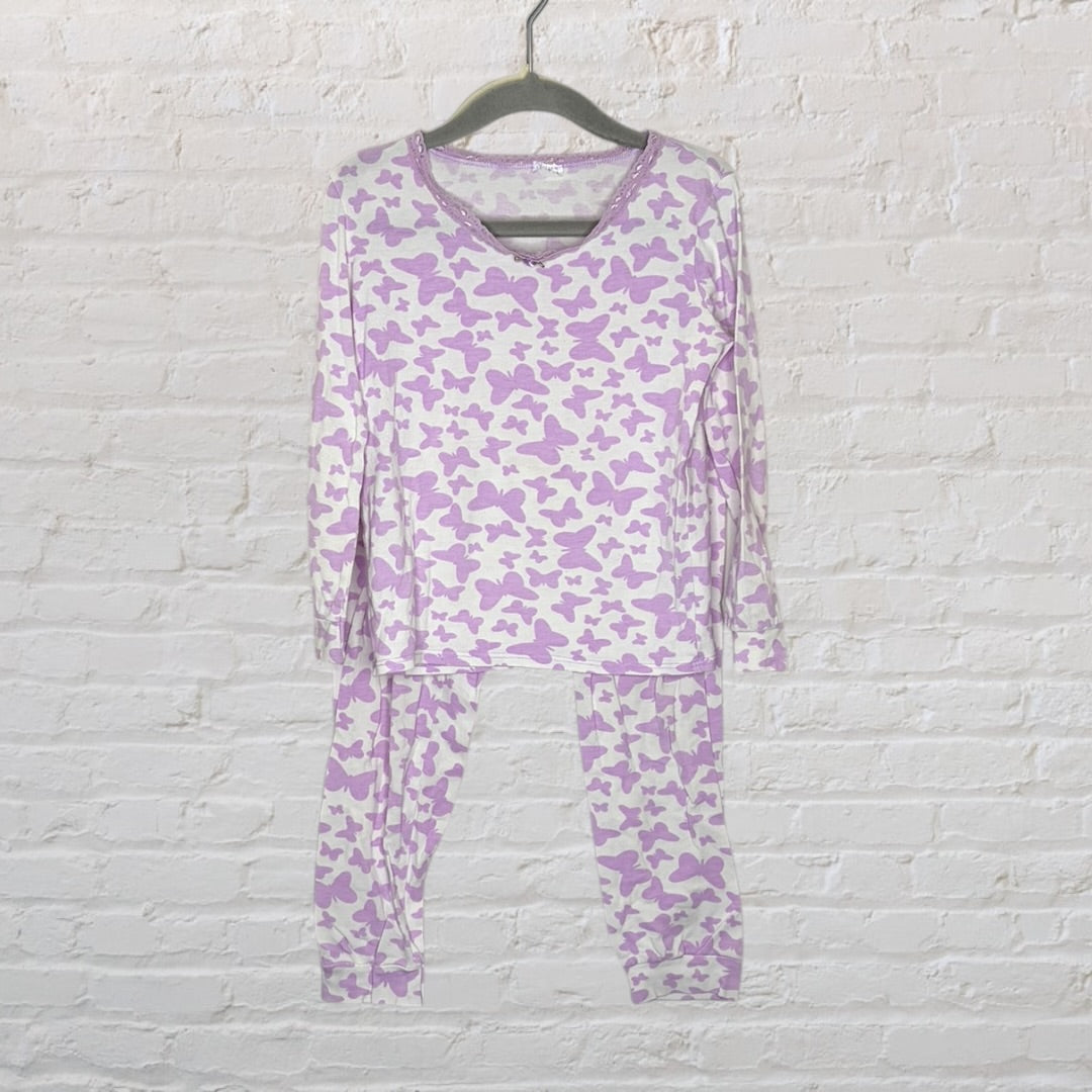 White and purple butterfly print pajama set with long sleeves and pants, displayed on a hanger against a brick wall.