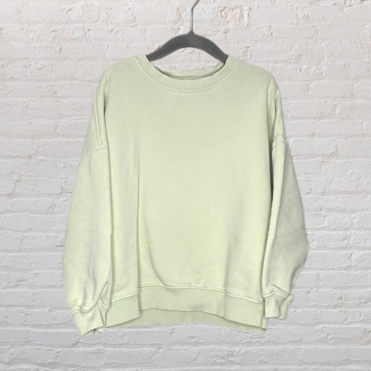Light mint green oversized sweatshirt on a black hanger against a white brick wall background.