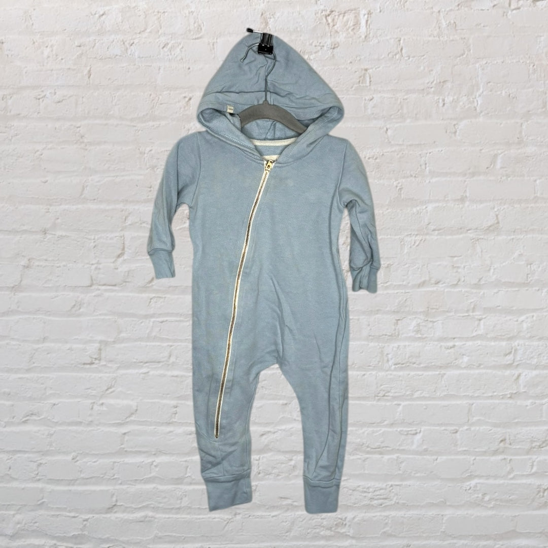 Light blue hooded baby romper with a diagonal zipper, hanging against a white brick wall.