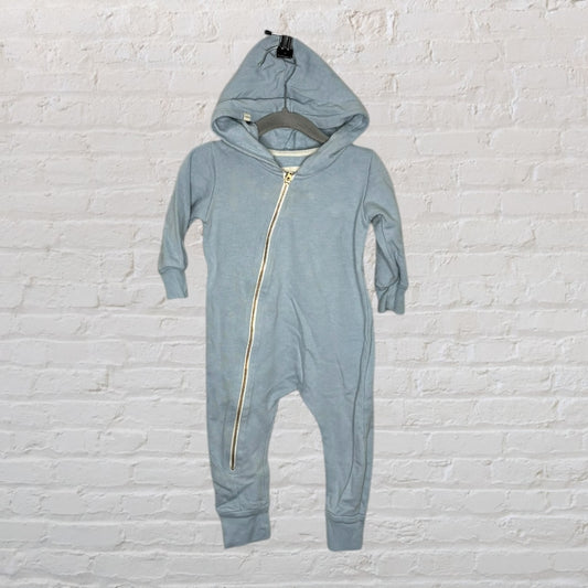 Light blue hooded baby romper with a diagonal zipper, hanging against a white brick wall.