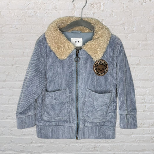Light blue corduroy jacket with beige sherpa collar and decorative patch, made by Hux, on a hanger.