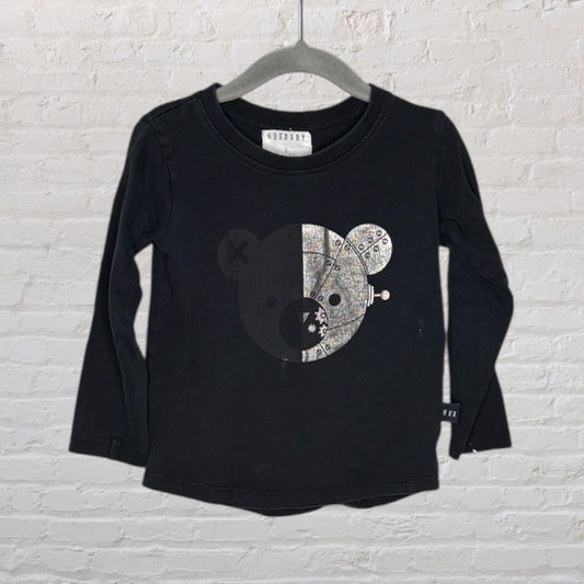 Black long sleeve tee with a graphic bear design, displayed on a hanger against a white brick wall.