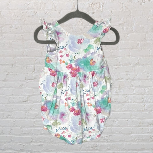 A multicolored floral print baby romper with ruffled sleeves, hanging on a black hanger against a white brick wall.