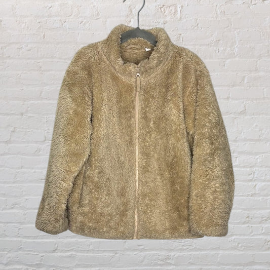 Beige teddy fleece jacket with a zip-up front, hanging on a hanger against a brick wall.