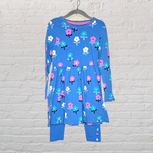 Blue dress with colorful floral print and matching leggings hanging on a hanger against a brick wall.